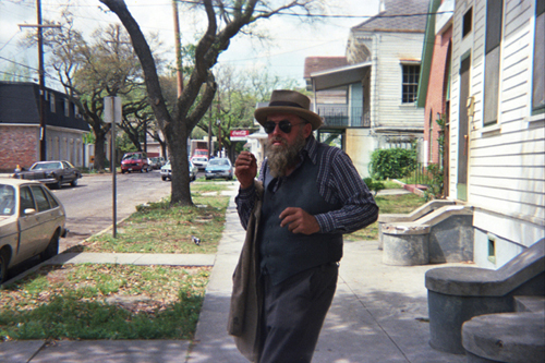 Poppa Neutrino walking down a suburban street wearing a hat
