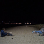 Teenage boy with a video camera films a derelict on a beach at night