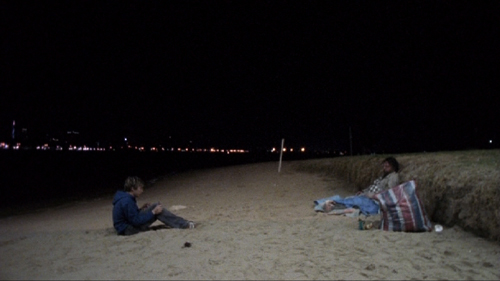 Teenage boy with a video camera films a derelict on a beach at night