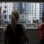 Teenage boy with a video camera stands on a bridge overpass talking to two girls