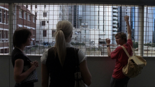 Teenage boy with a video camera stands on a bridge overpass talking to two girls