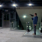 Young man holding a video camera stands next to an elevator