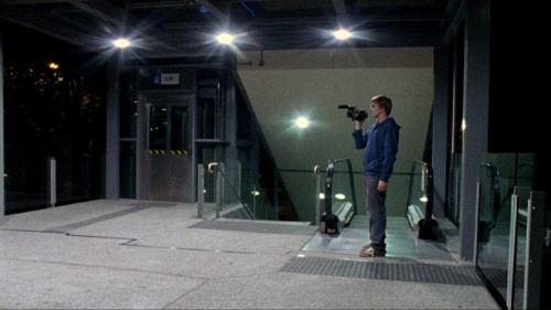 Young man holding a video camera stands next to an elevator