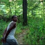African American teenage boy with his hands tied togethre runs for his life through the woods