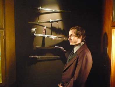 Creepy guy standing in front of wall of weapons