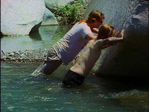 Two men doing push-ups against a rock in a pond