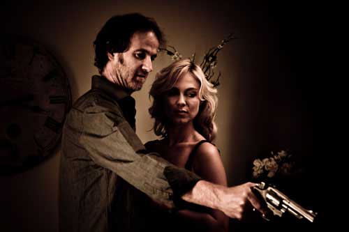 Man points a gun while standing next to a beautiful blonde woman