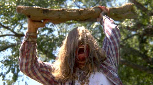 Man with long hair wields branch over his head