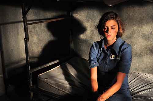 Female convict sits on her bunk