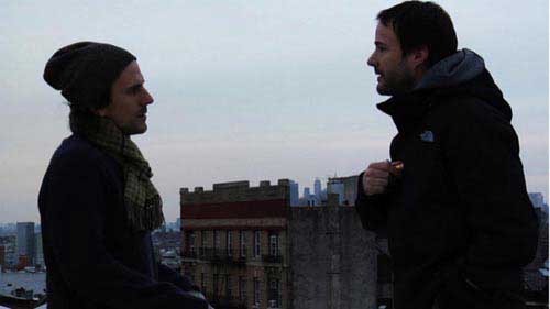 Two male friends talk on an urban rooftop