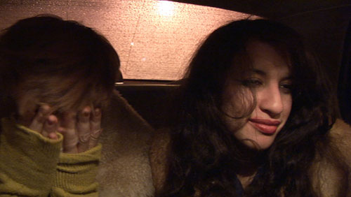 Two women sit close to each other in the backseat of a taxi cab