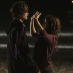 Girl puts blindfold on boy on the beach at night