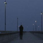 Man walks down a pier on the ocean at night