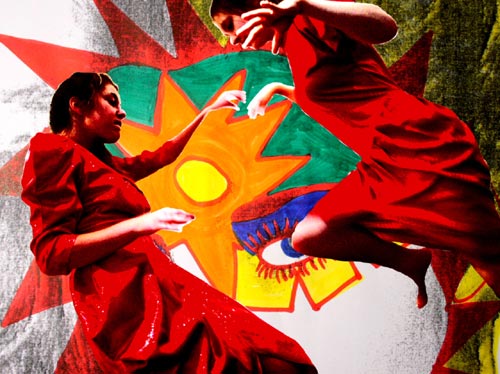 Two teenage girls in red dressed dance in front of artwork
