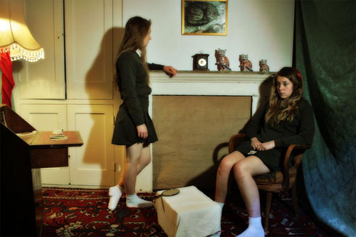 Two teenage girls dressed in schoolgirl outfits look morose