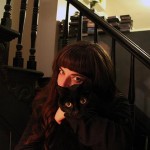 Filmmaker Christine Lucy Latimer hugs her black cat Mingus in front of a staircase