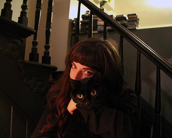 Filmmaker Christine Lucy Latimer hugs her black cat Mingus in front of a staircase