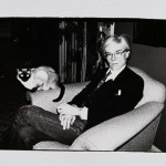 Artist Andy Warhol sits in a chair with a siamese cat