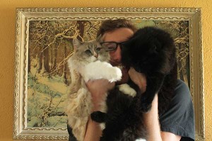 Filmmaker Ben Popp holds his two cats, one white and one black, up to his face