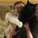 Ben Popp's face is covered by his two cats, one white and one black