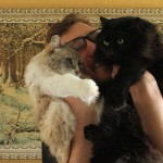 Ben Popp smiles while he rubs his two cats, one white and one black, on his face