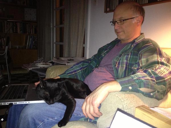 Filmmaker Jeff Krulik tries to work on his laptop while his black cat Iggy sleeps on his legs