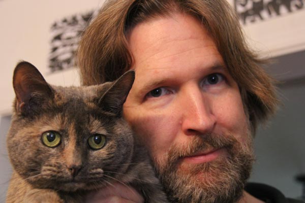Filmmaker Skizz Cyzyk holds up his cat Speck, who has a concerned look on her face