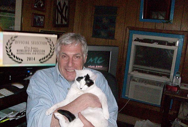 Filmmaker Vic Zimet sits in front of his computer workstation while holding his white cat Fidget