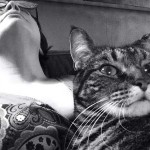 Lisa Barcy leans back on her couch while her cat Nellie rests on Lisa's stomach in this black and white photograph