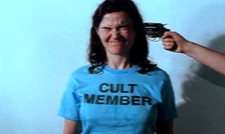 Mind Control Made Easy Woman wearing a t-shirt that says "Cult Member" has a gun pointed at her head