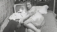 Woman lying in bed with a man who has a TV for a head