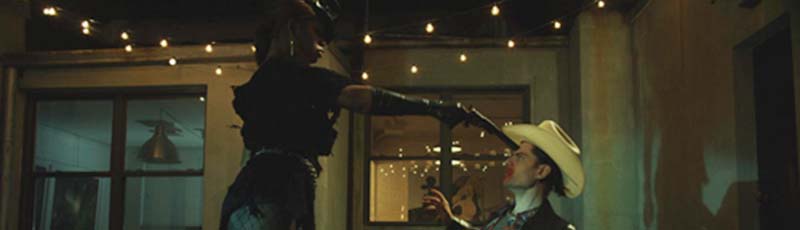 Laverne Cox points a gun at the head of a man wearing a cowboy hat