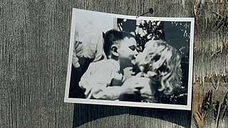 Old B&W photo of a boy kissing a young girl that is nailed to a piece of wood