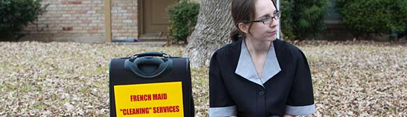 A housecleaner sits on a suburban curb with her suitcase