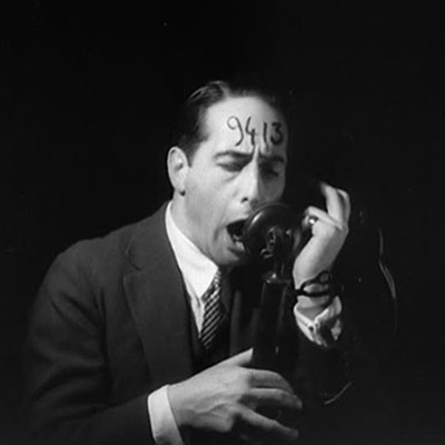 A man with the number 9413 written on his forehead yells into a telephone in Robert Florey/s film The Life and Death of 9413 — A Hollywood Extra