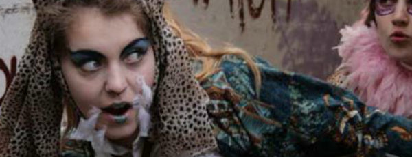 Two teenage girls dressed in outlandish costumes run down a dirty alley