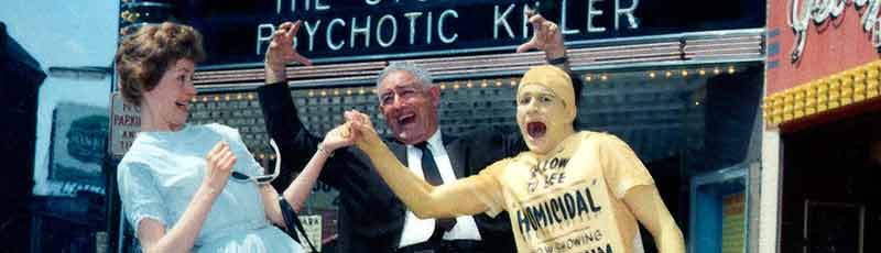 William Castle under a movie marquee with two actors