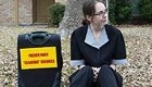 Maid sitting on a suburban curb with her suitcase